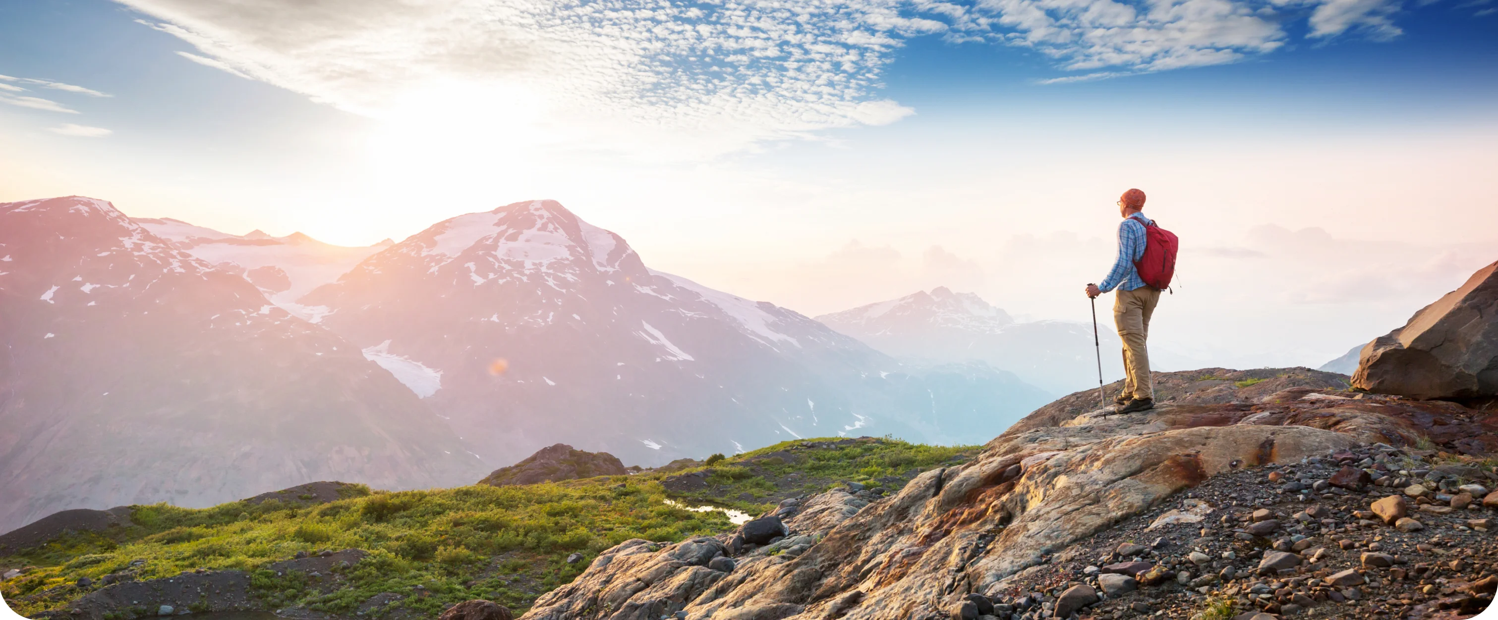 Hiker with trekking poles looking out over snow-capped peaks at sunrise
